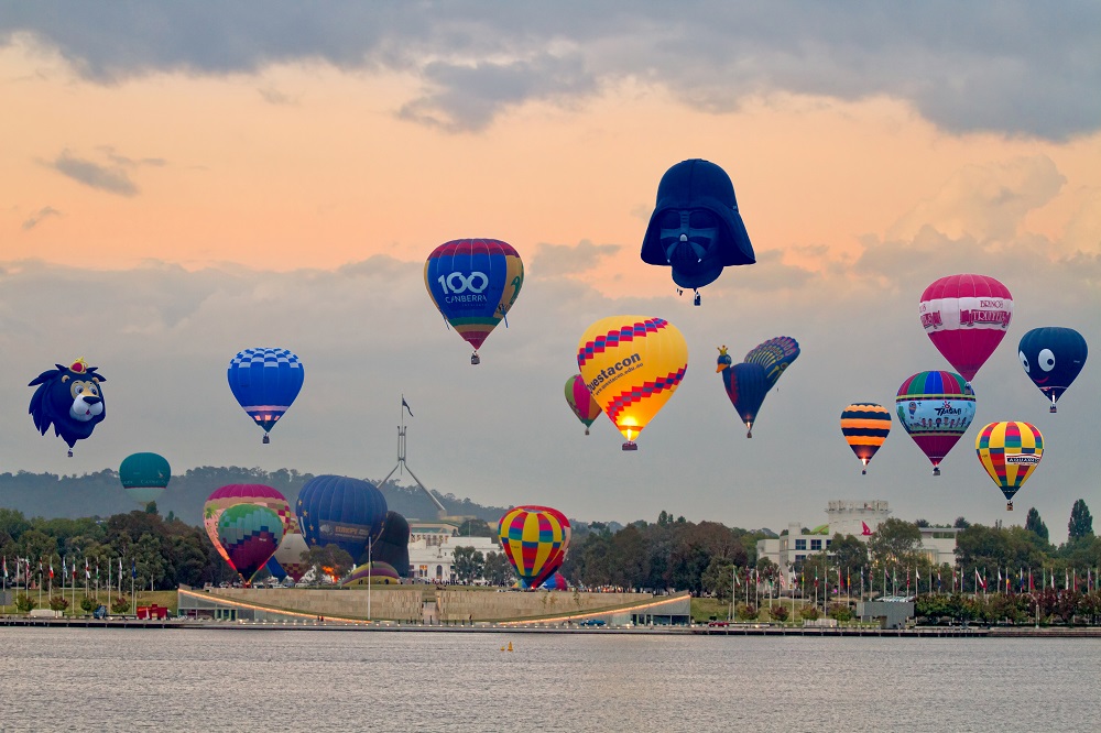 Various hot air balloons taking off over Lake Burley Griffin with parliament house in the background