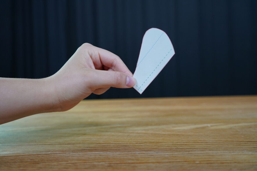 A hand holds a cut-out paper template in the shape of a wing. This is the seed spinner.