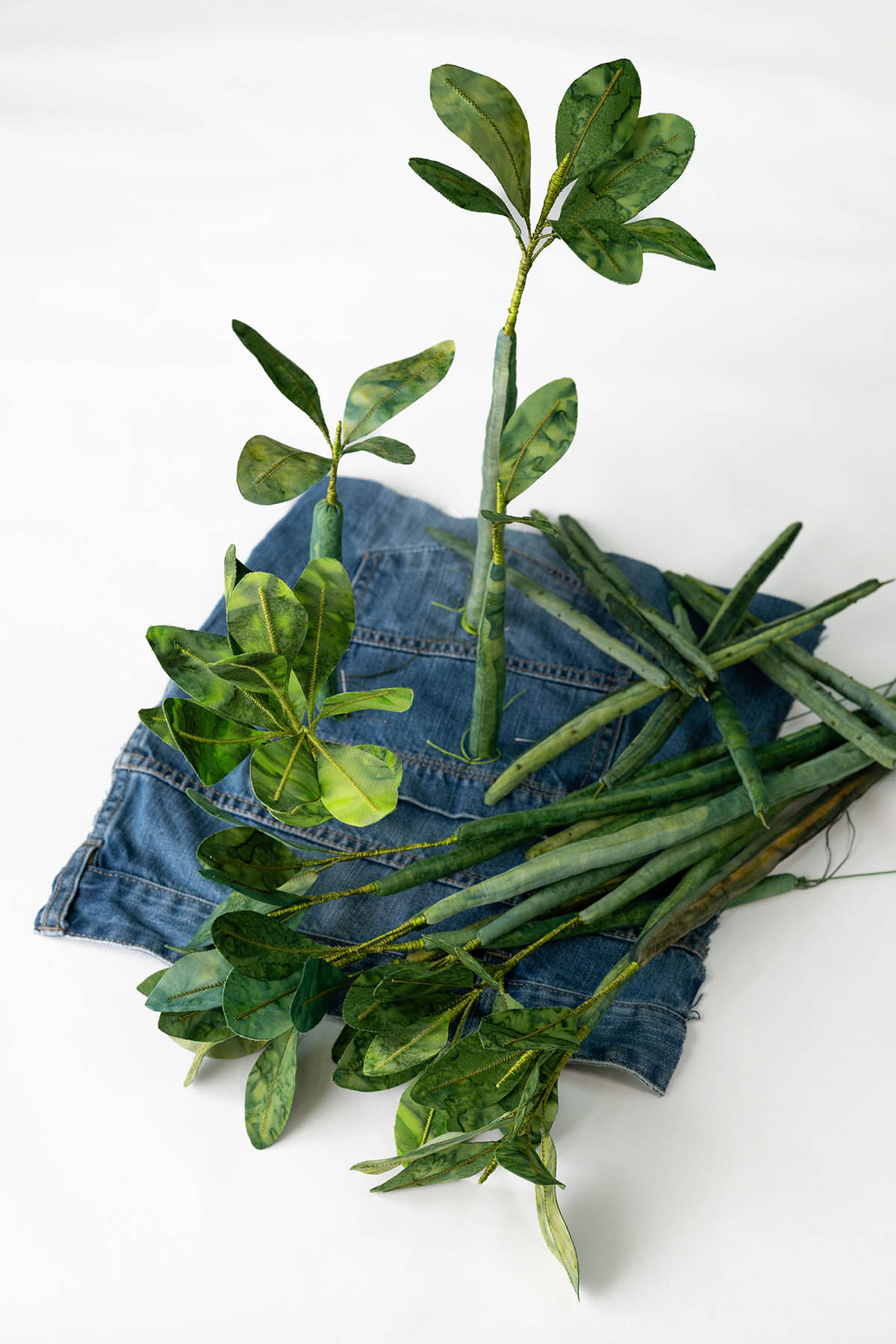 A close-up image of a denim patchwork quilt created by artist Jasmine Jan. The quilt features an embroidered crab, and an illustrated picture of a bird.