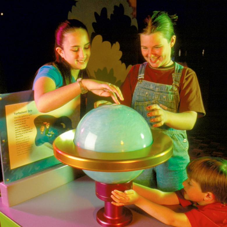 Three children stand around a spinning sphere