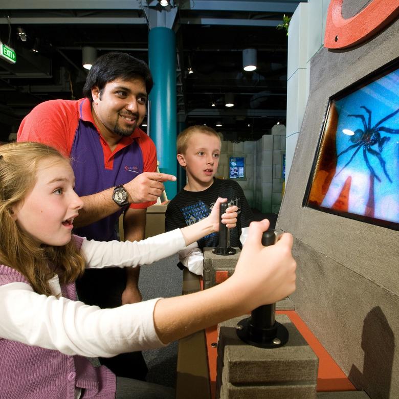 Three children and a Questacon staff member look at an image of a spider