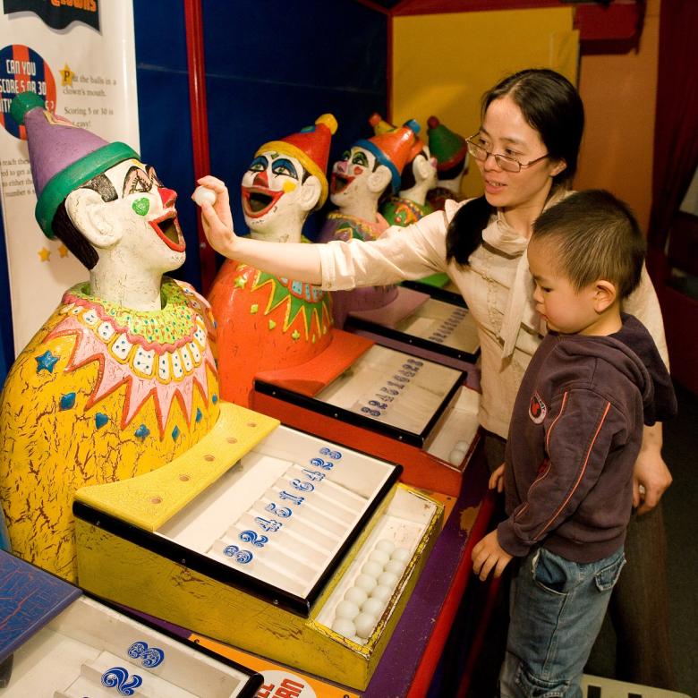 A mother and child place balls in a clown's mouth