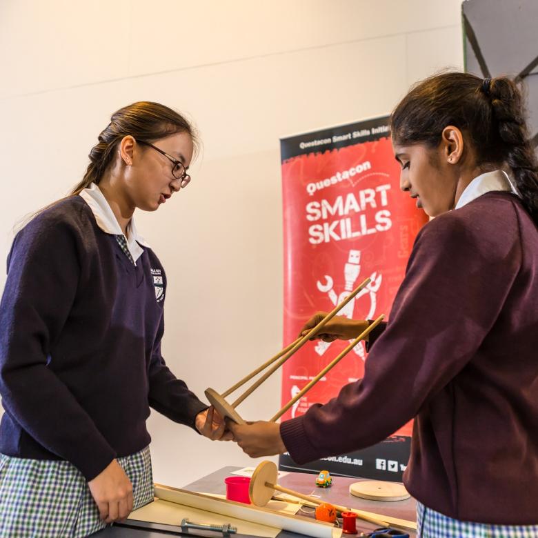 Two students build a structure from wooden sticks