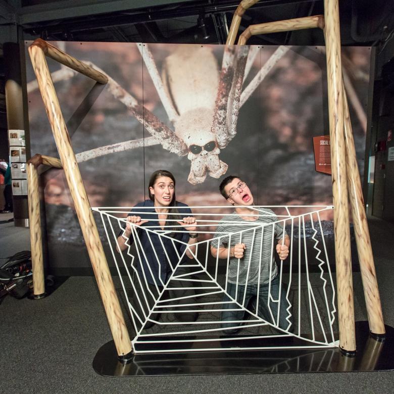 Two people pose behind a giant fake spider web