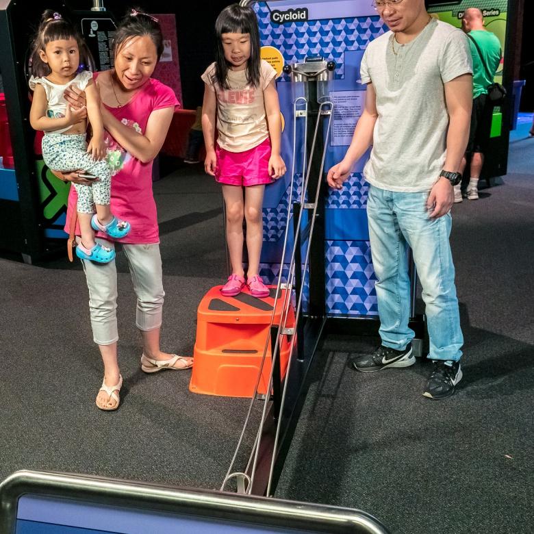 A family watch a ball roll down a curved ramp