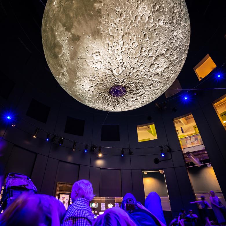 People lay underneath a model of the Moon