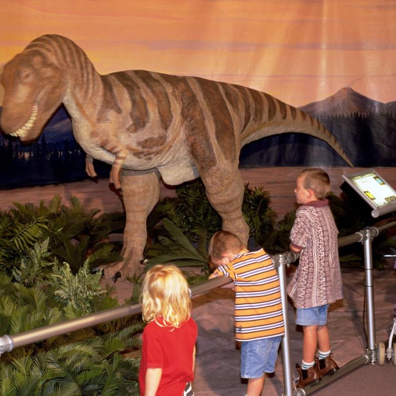 A family in nineties fashion look up at a statue of a T-rex.