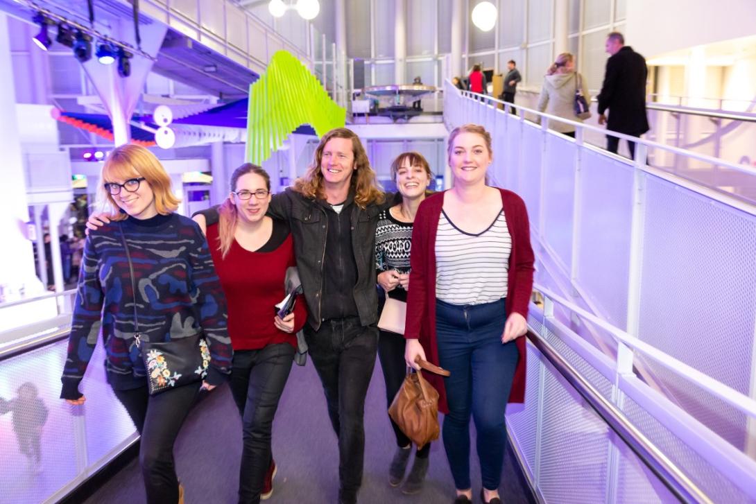 Five people dressed in jeans and jumpers walk towards the camera smiling