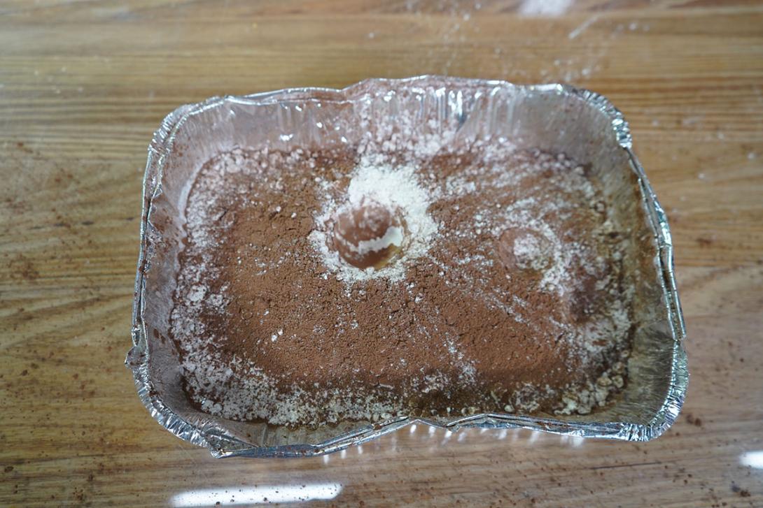 The surface flour and cocoa powder has small round crater on the right side of the tray and a larger, deeper cater in the centre.